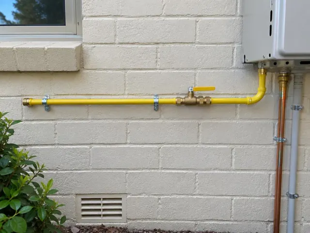 Yellow gas pipe and shutoff valve on an exterior brick wall beside an appliance in Manly Vale